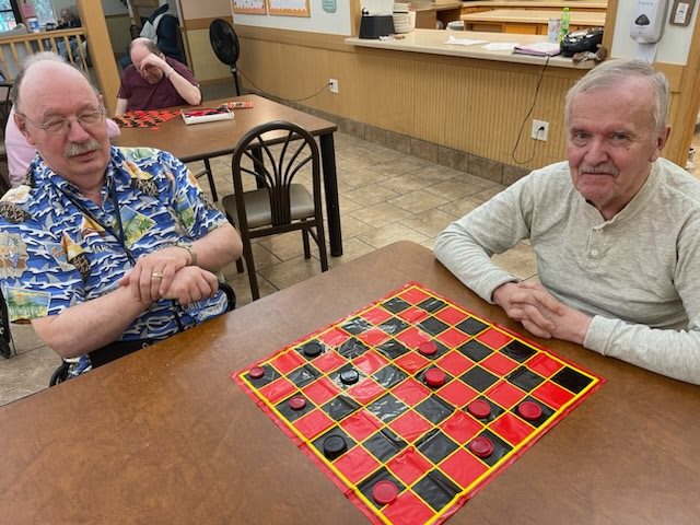 Two elderly men playing a game of checkers in a community center.