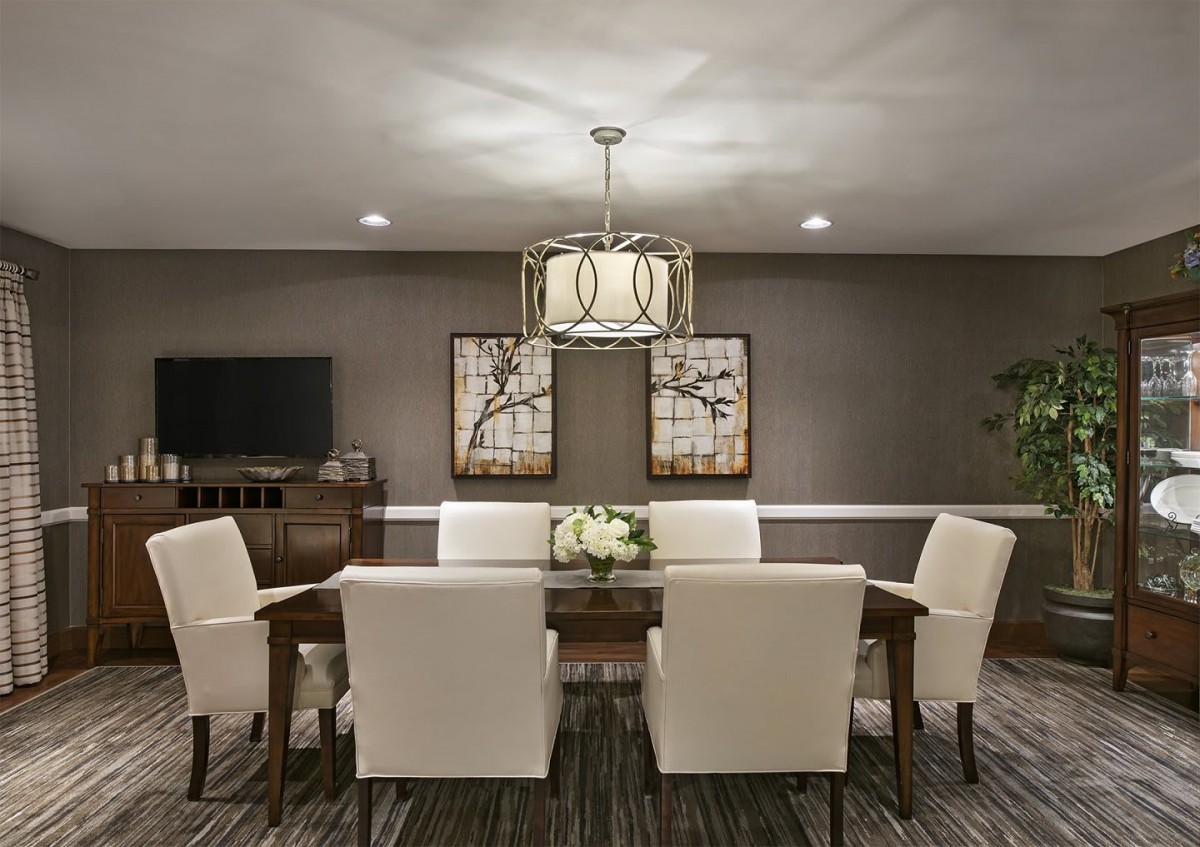 A modern dining room with elegant decor, featuring a central chandelier, a wooden dining table surrounded by upholstered chairs, and decorative wall art.