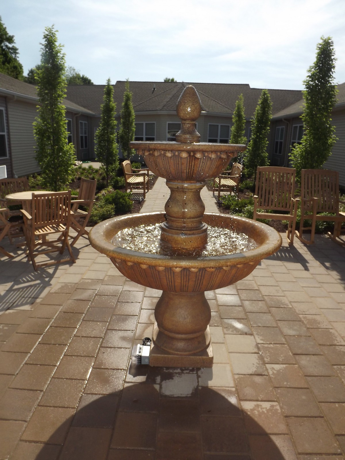 A tranquil courtyard with a central fountain surrounded by seating areas under the daytime sun.