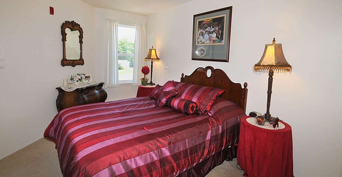 A cozy bedroom featuring a striped red bedspread, adorned with matching pillows, a lamp on the side table, and a framed picture above the headboard.
