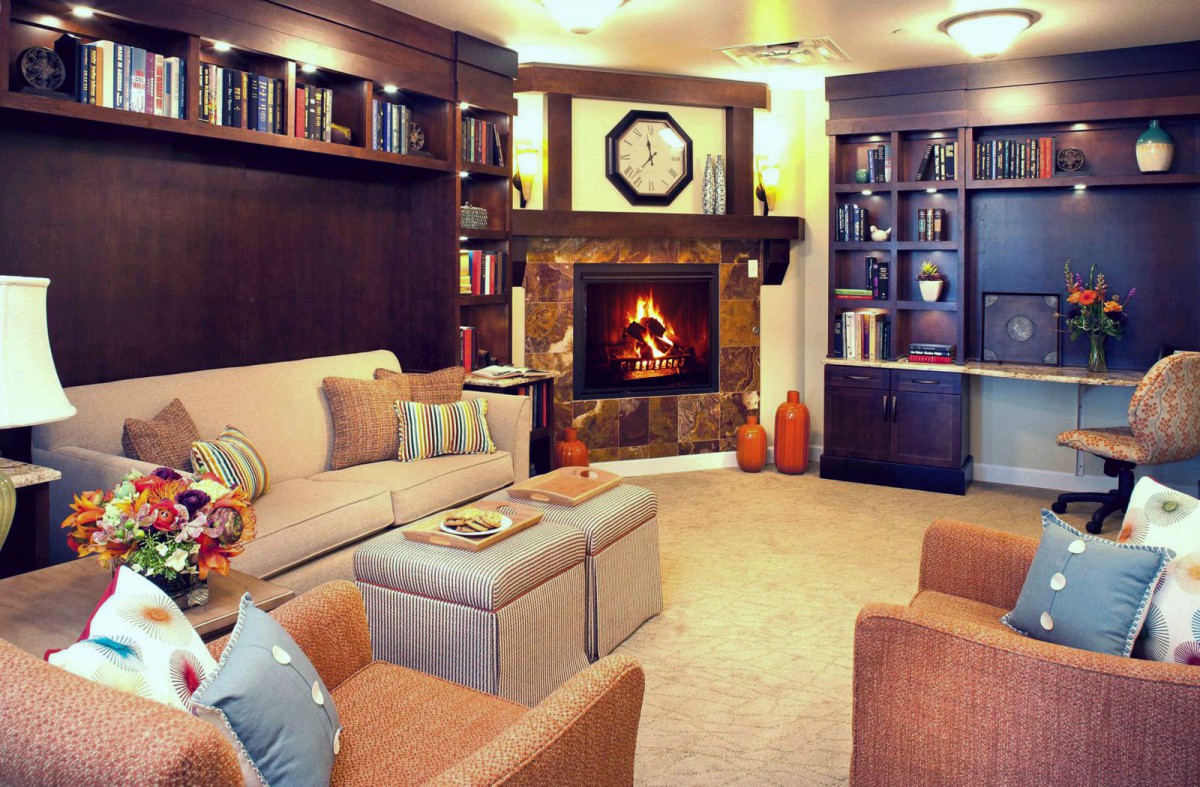 A cozy living room with a warm fireplace, surrounded by bookshelves and comfortable seating.