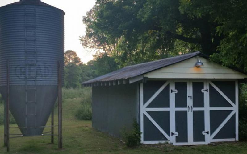 A small barn next to a silo in a rural setting during sunset.