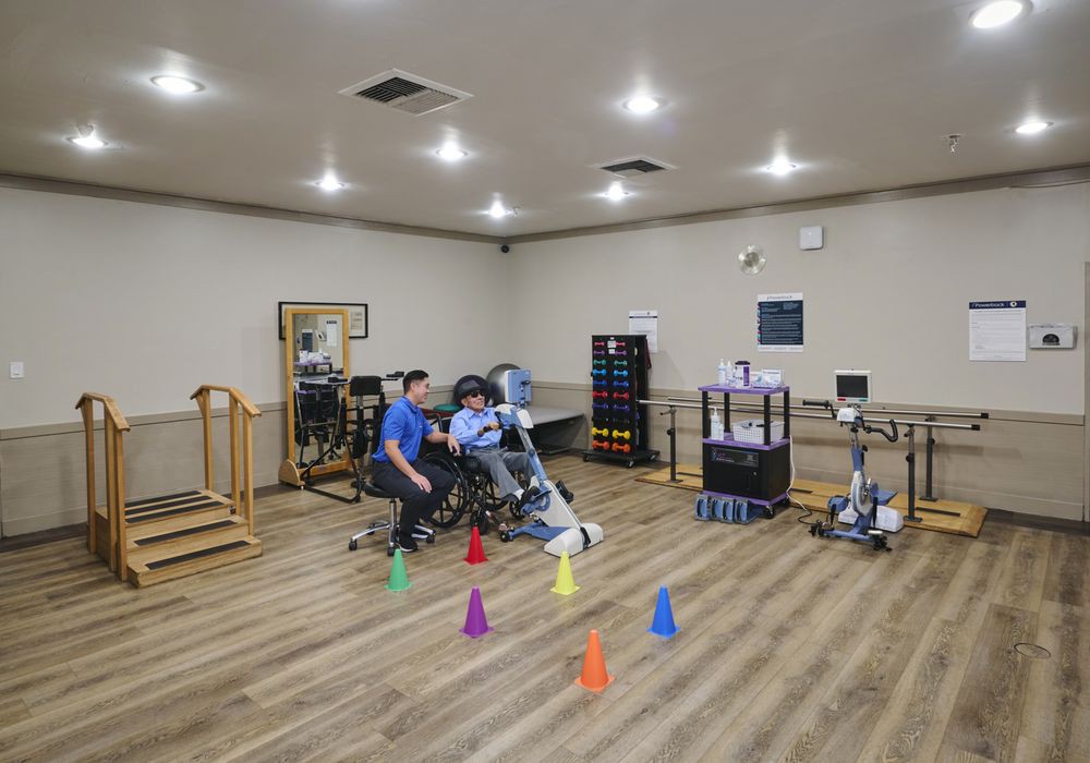 A physical therapy session with a therapist assisting a person on exercise equipment in a rehabilitation gym.