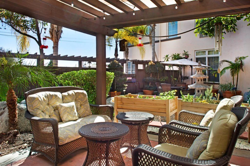 A cozy outdoor patio with comfortable seating and a pergola surrounded by lush greenery.