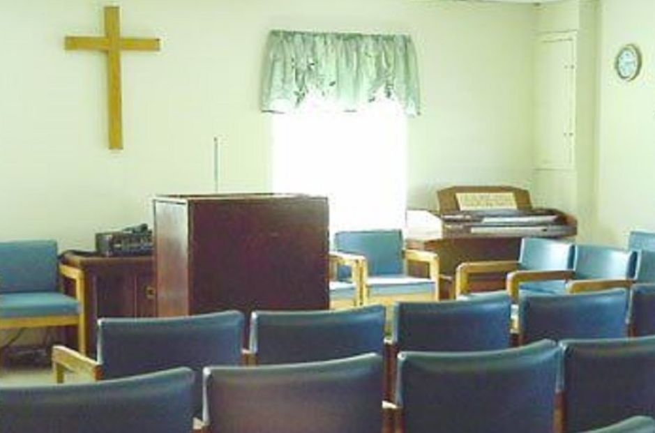 An interior view of a small church with a pulpit, seating, and an organ.