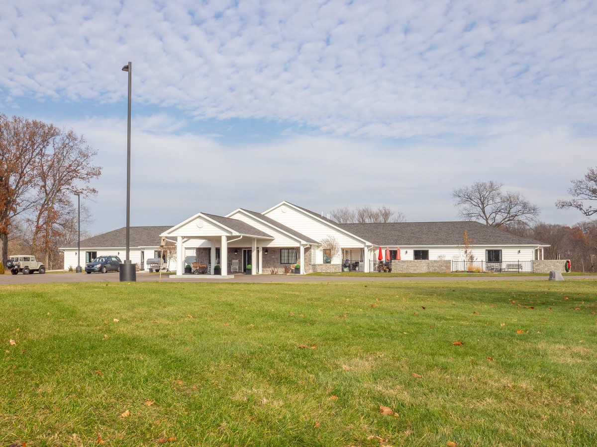 A single-story building with a large grassy area in front, under a partly cloudy sky.