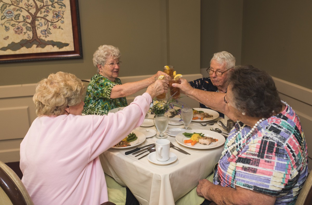 A group of elderly friends enjoying a meal and toasting at a dining table.