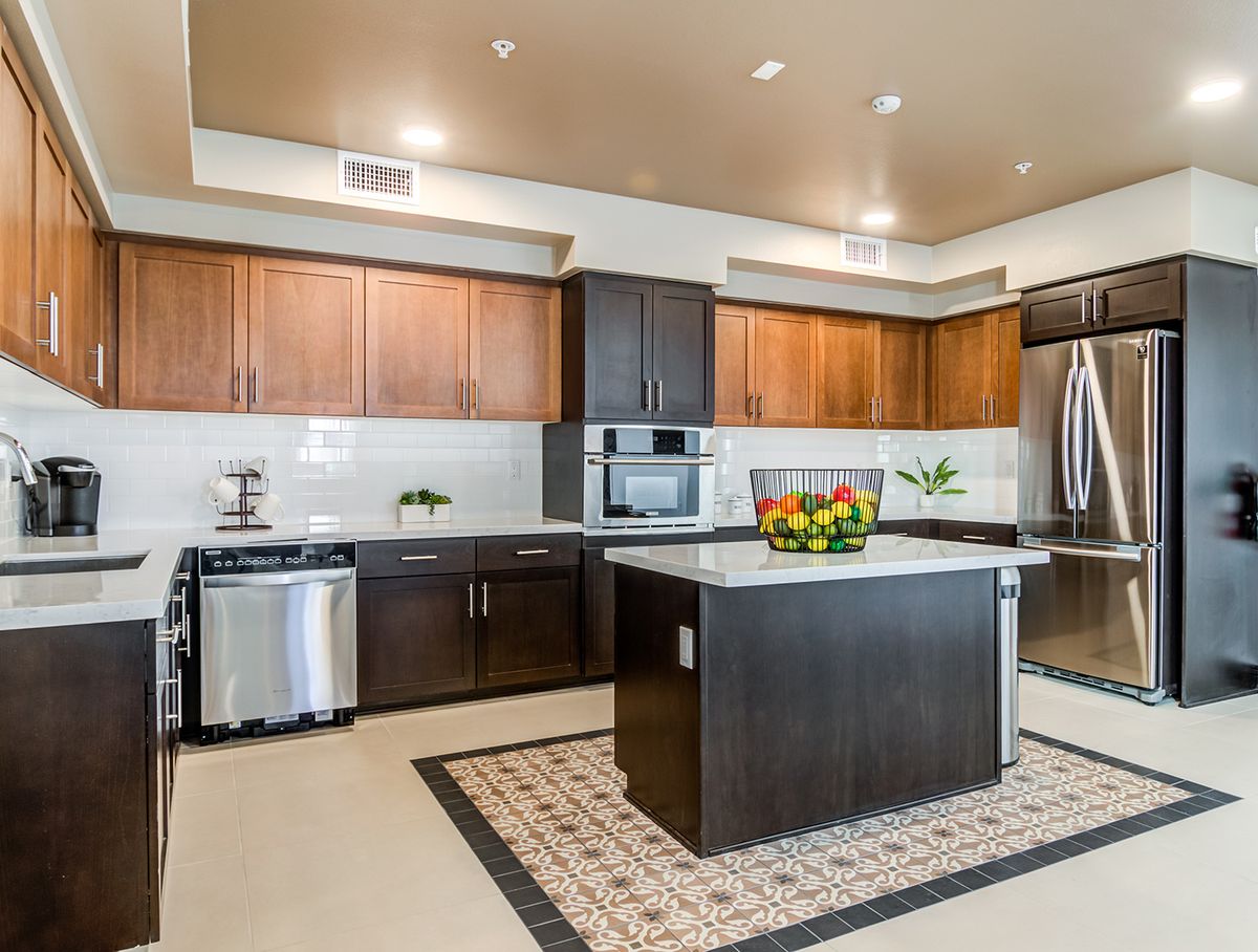 A modern kitchen with wooden cabinets and a central island, featuring stainless steel appliances and a fruit bowl.