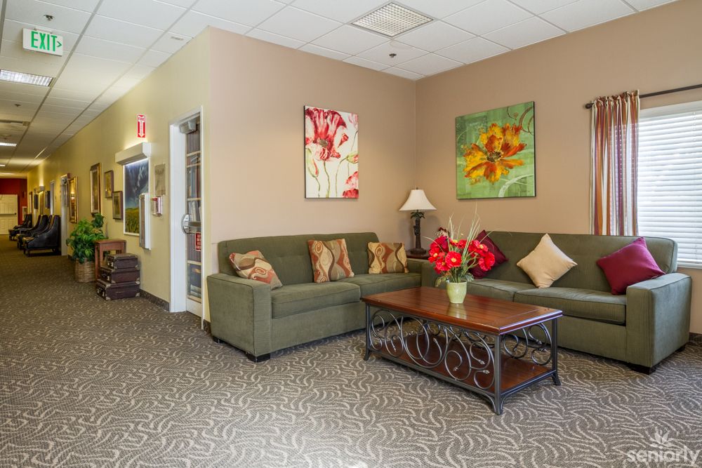 A cozy living room with green couches, a wooden coffee table, and colorful artwork on the walls.