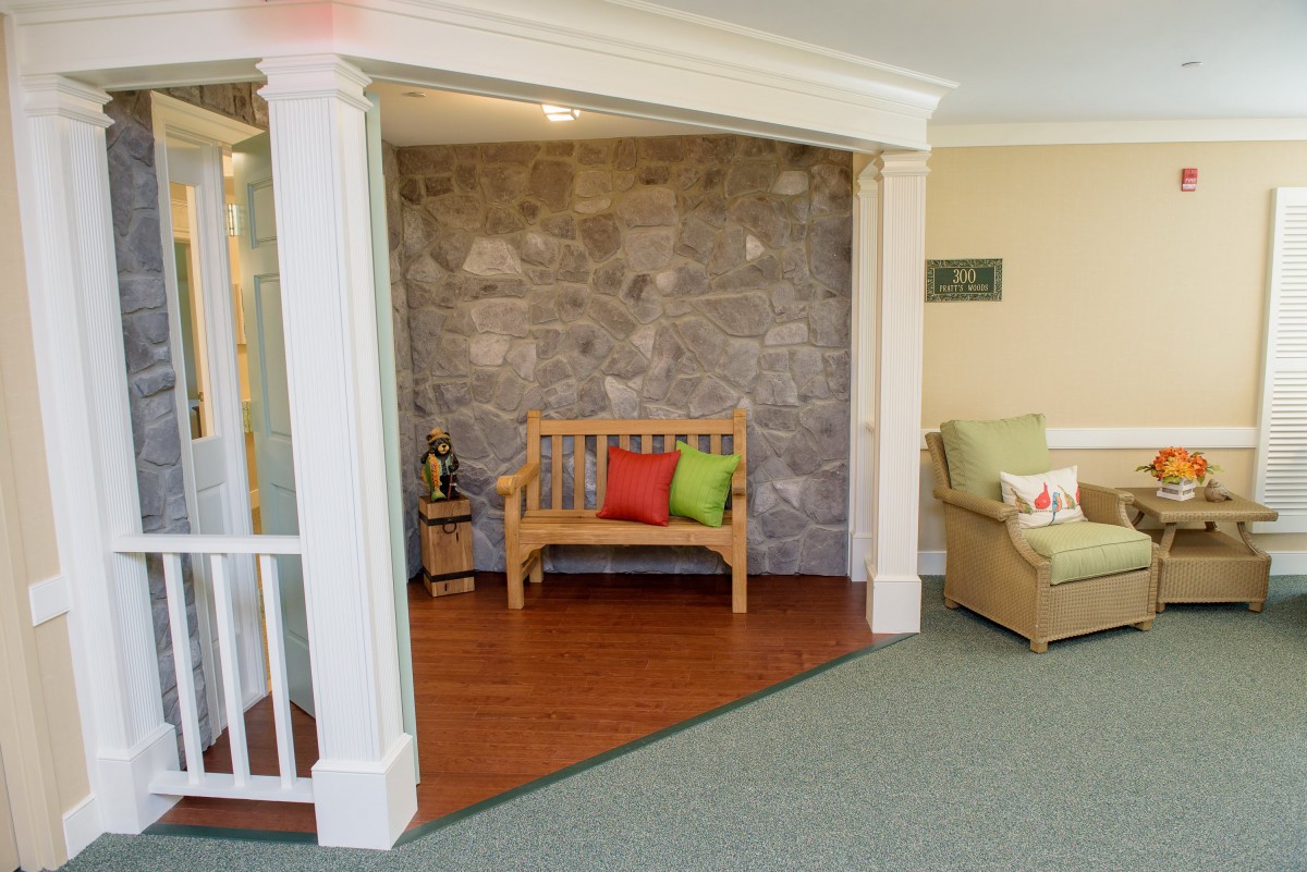 A cozy indoor seating area with a wooden bench, colorful cushions, and a stone wall backdrop.