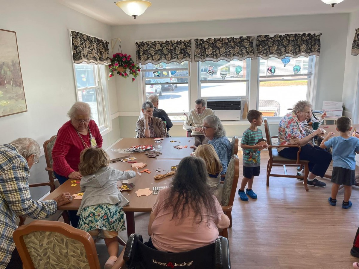 A group of seniors and children are gathered indoors, socializing and playing cards together.