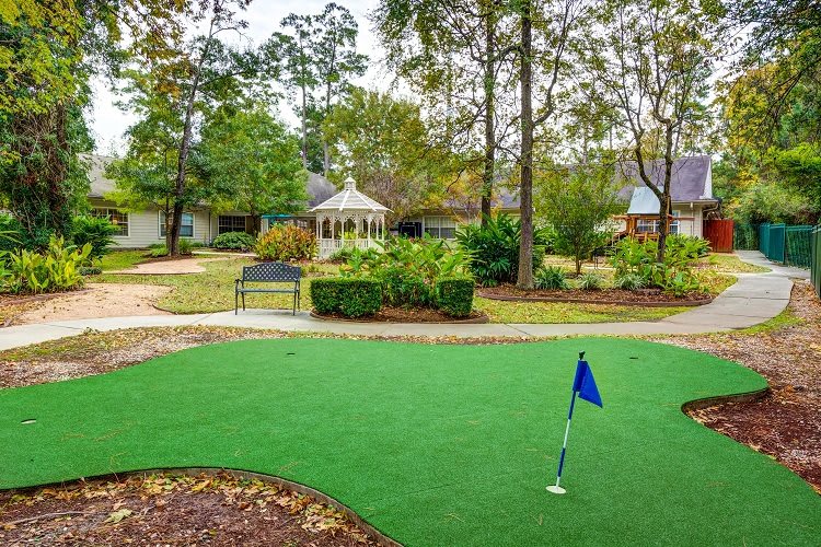A tranquil outdoor garden with a gazebo, surrounded by trees and a manicured lawn.