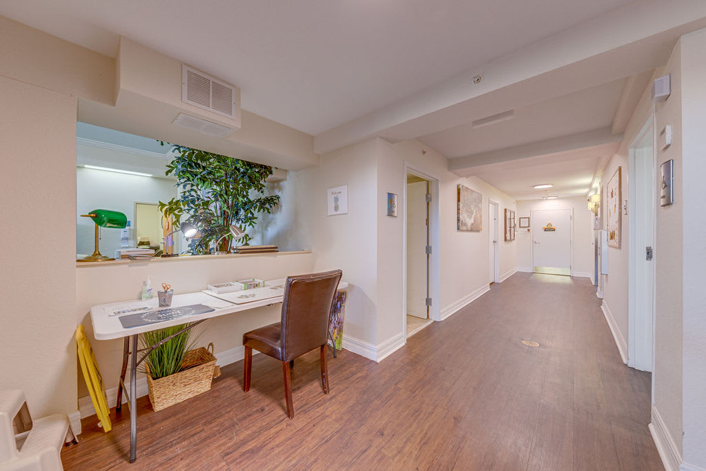 An office hallway with a desk and chair, featuring decorative plants and artwork.