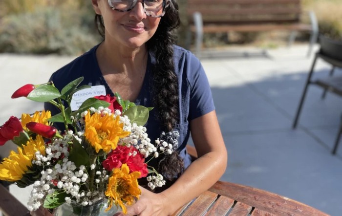 A woman with glasses and a braid, holding a bouquet of colorful flowers outside.