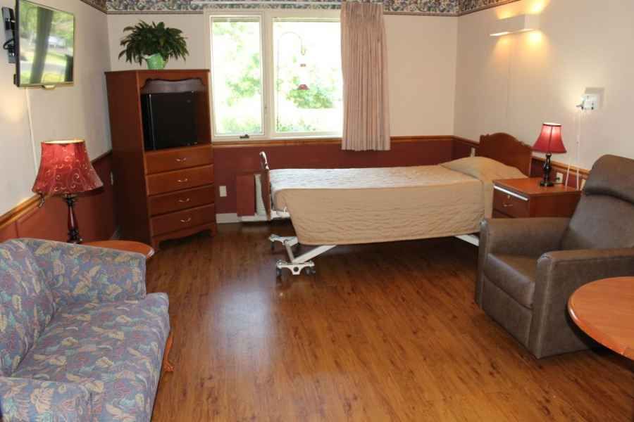 A hospital room with a bed, television, and wooden flooring.