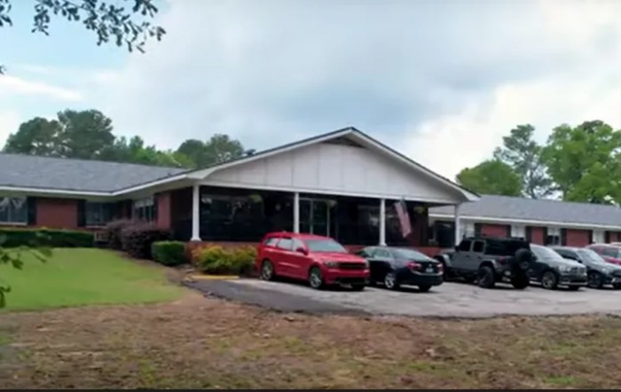 A residential building with several cars parked in the driveway under a cloudy sky.