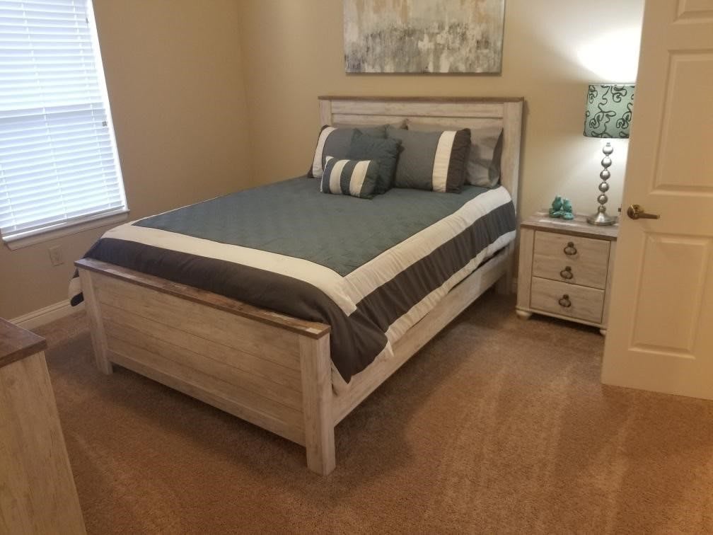 A cozy bedroom with a neatly made bed and a nightstand with a lamp.