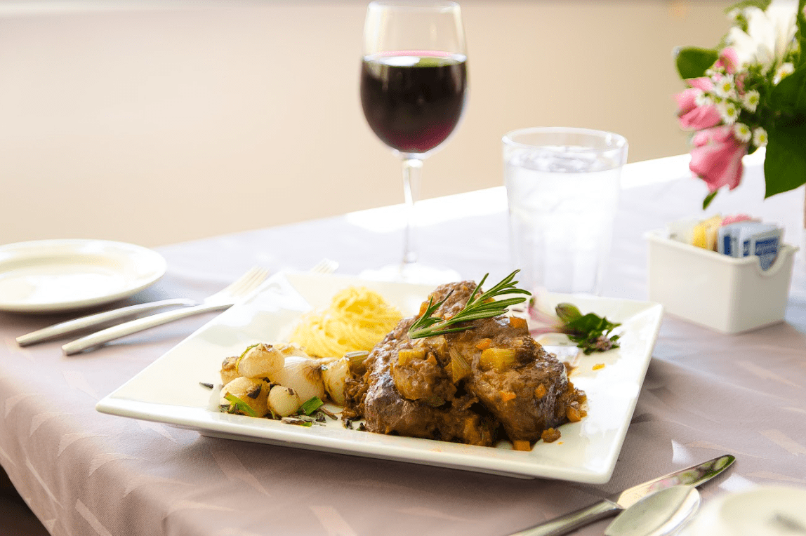 A plated meal featuring meat, potatoes, and vegetables, accompanied by a glass of red wine on a dining table.