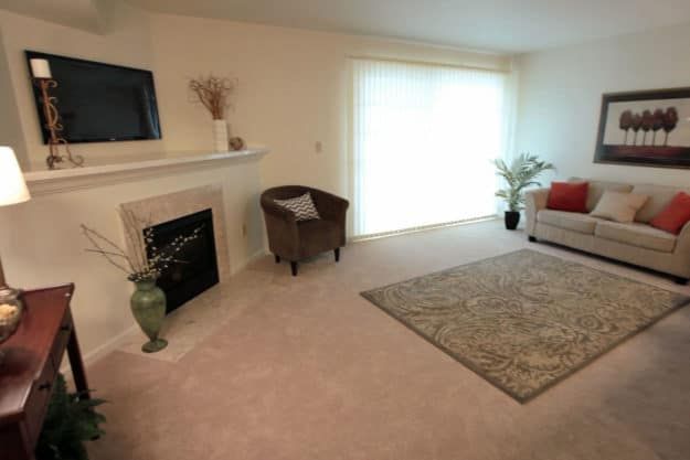 A minimalist living room with a fireplace, armchair, and sofa, illuminated by natural light from large sliding doors.