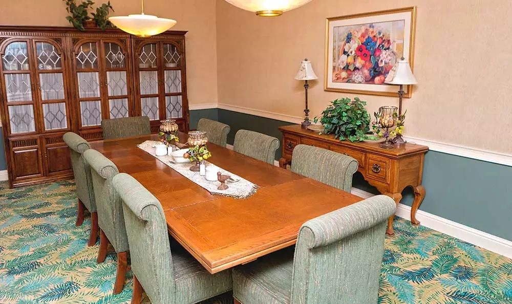A traditional dining room featuring a large wooden table surrounded by upholstered chairs, adorned with decorative elements and a lamp.