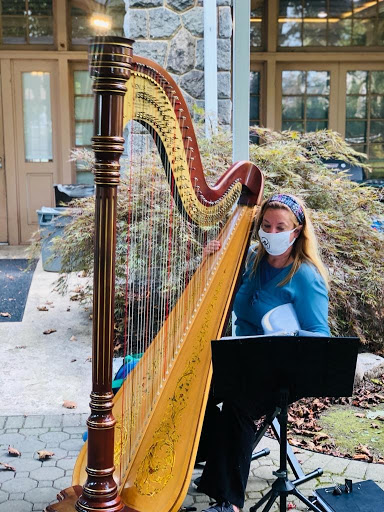 A musician plays the harp outdoors while wearing a mask.