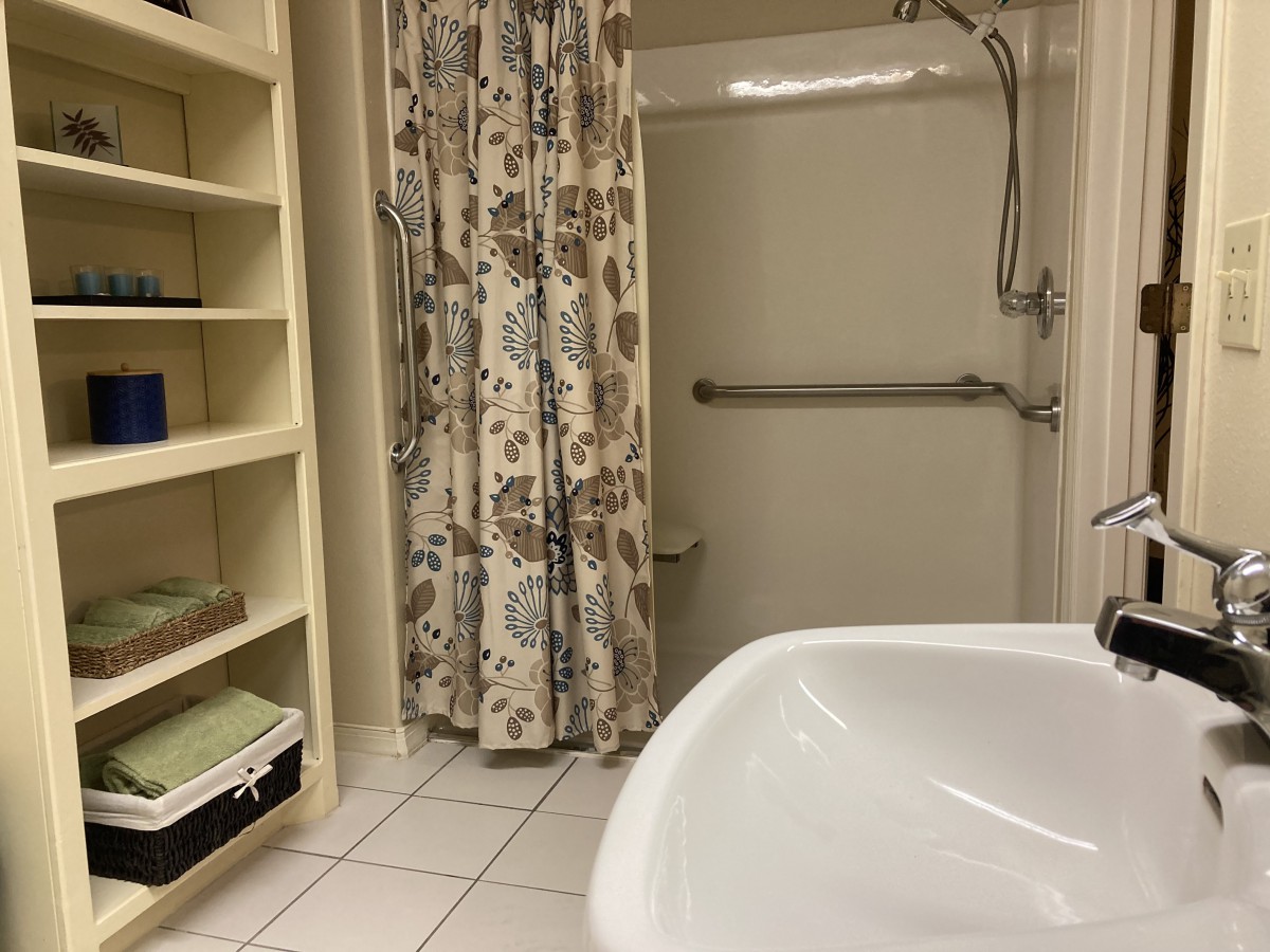 A cozy bathroom with a floral shower curtain, shelving, and neatly organized towels.