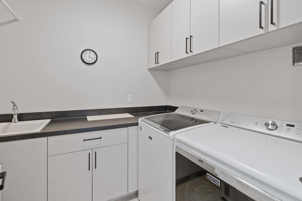 A modern laundry room with a washing machine, dryer, and storage cabinets.