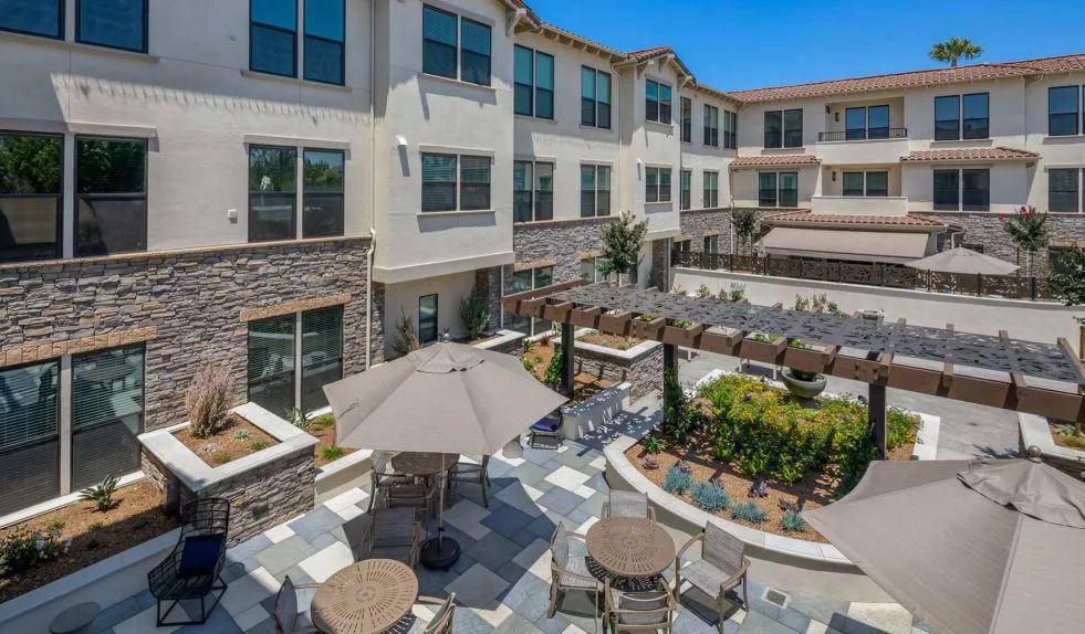A modern apartment complex featuring a landscaped courtyard with outdoor seating and patio umbrellas.