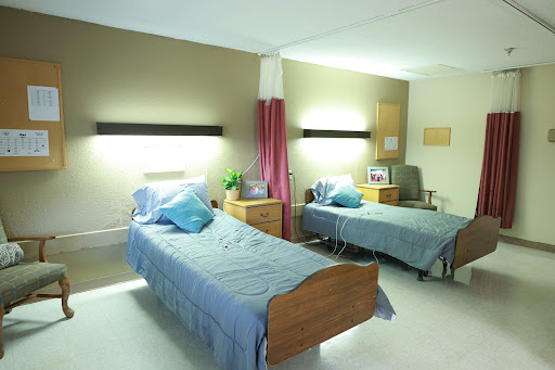 A view of a patient room featuring two hospital beds with bedside tables and soft lighting.