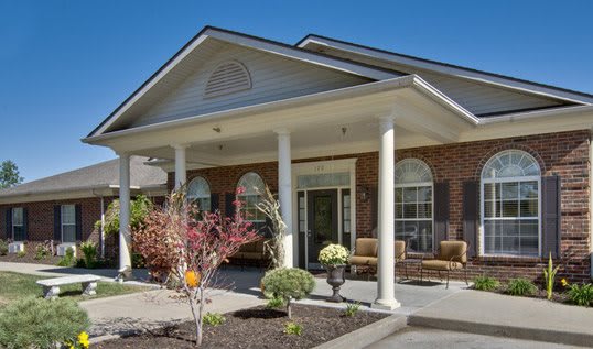 A residential house with a covered porch and white columns, surrounded by landscaping.