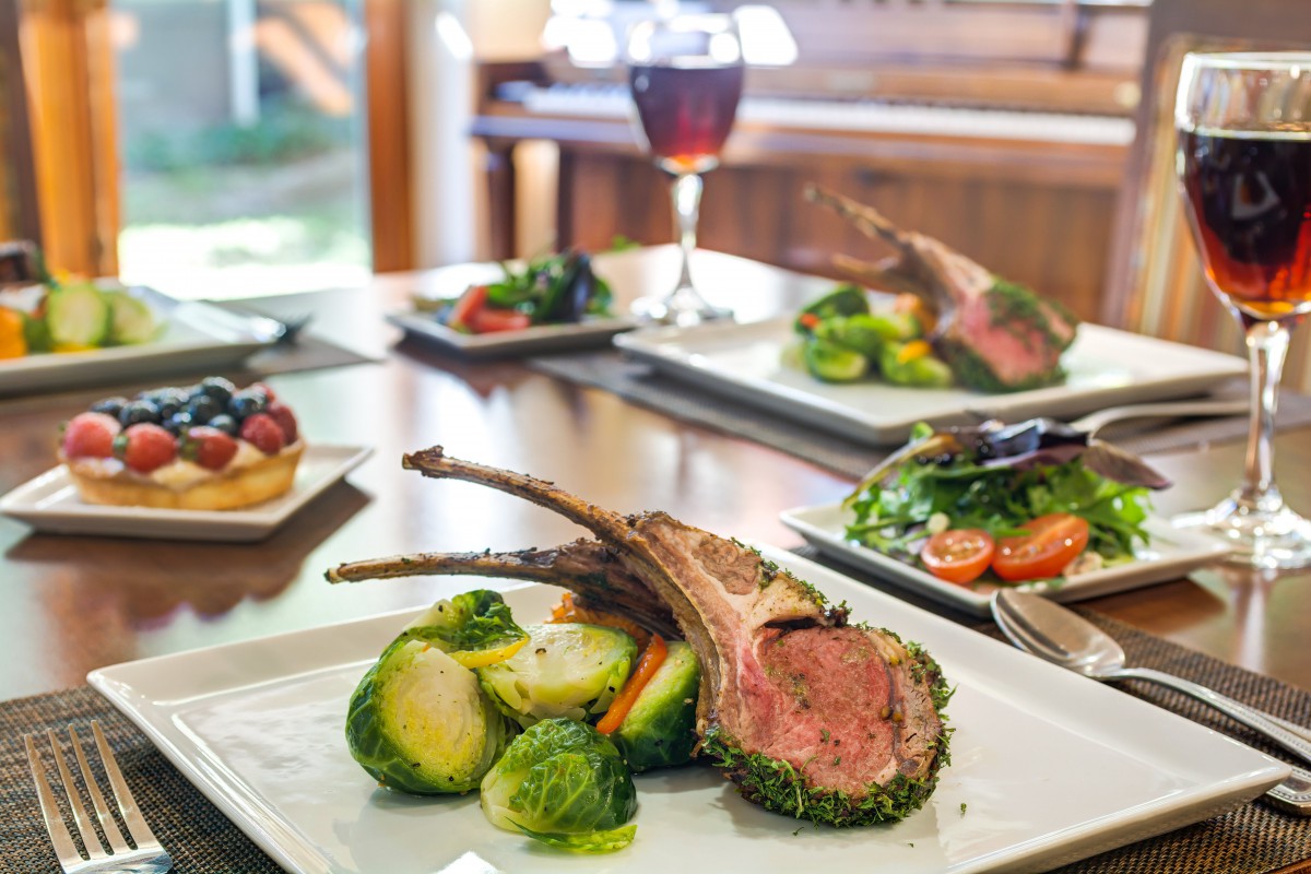 A gourmet meal featuring herb-crusted lamb chops and Brussels sprouts, accompanied by a glass of wine.