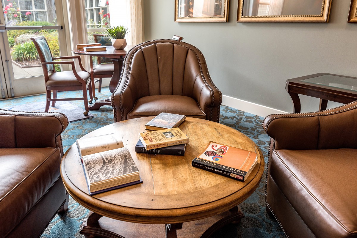 A cozy reading area with books on a round wooden table surrounded by leather chairs.