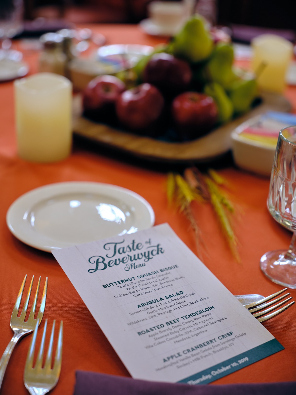 A beautifully arranged table with a menu, surrounded by elegant glassware and a fruit centerpiece.