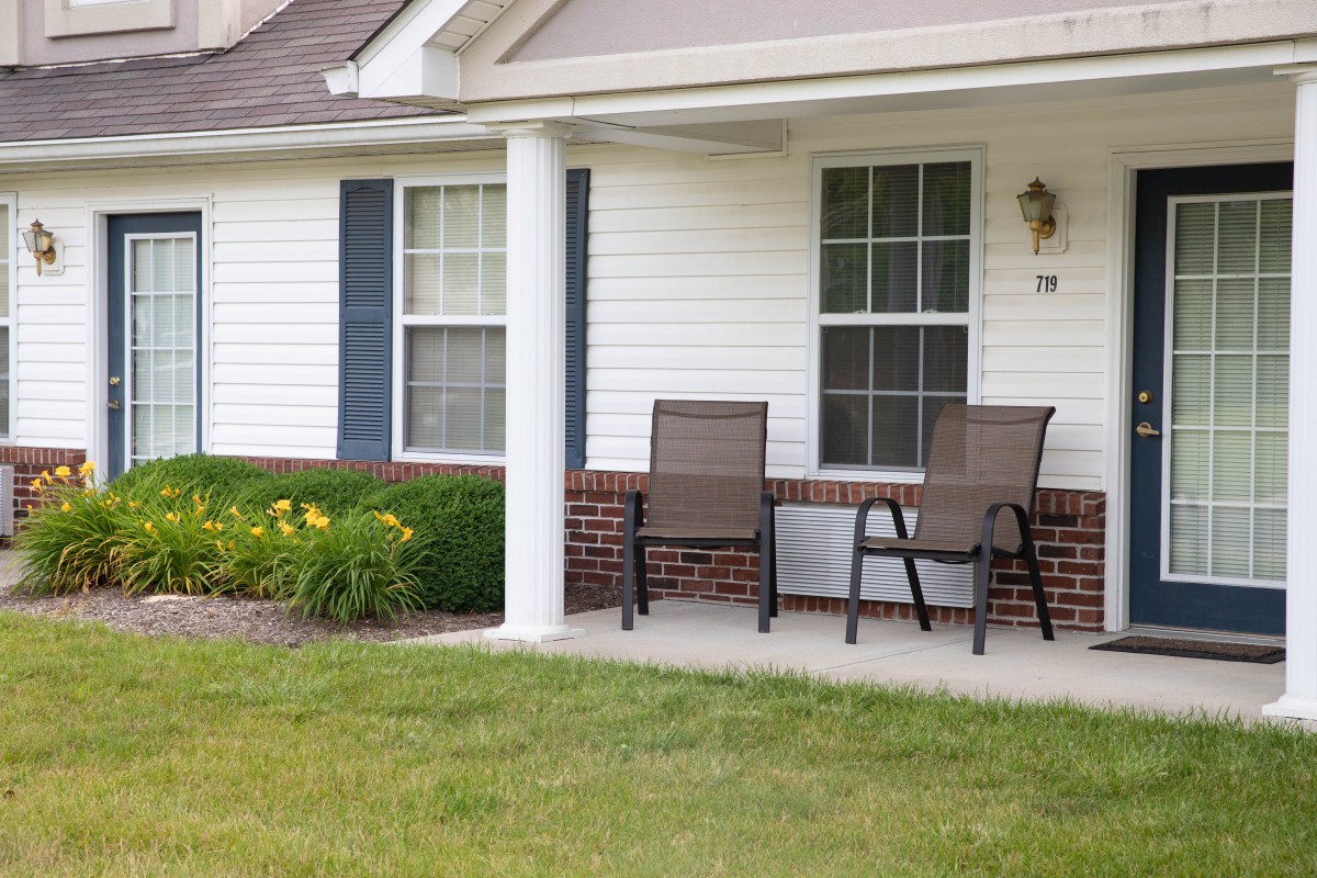 A cozy front porch with two chairs and a window, surrounded by a well-kept yard.