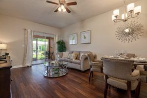 A cozy living room with a modern interior, featuring wood flooring and natural light streaming through large windows.