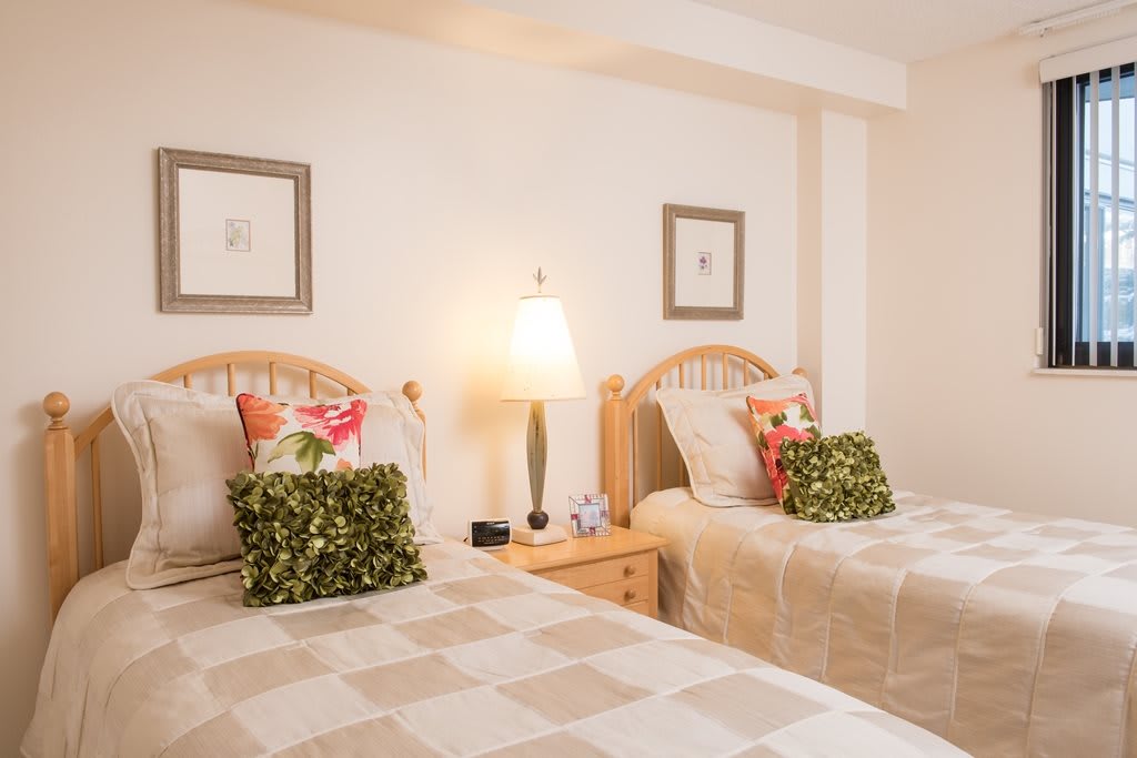 A cozy bedroom featuring twin beds with decorative pillows, a bedside lamp, and framed artwork on the walls.