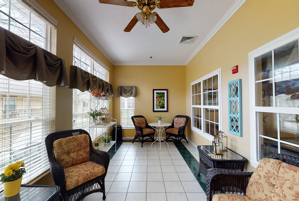 A cozy sunroom with wicker furniture, a ceiling fan, and large windows providing ample natural light.