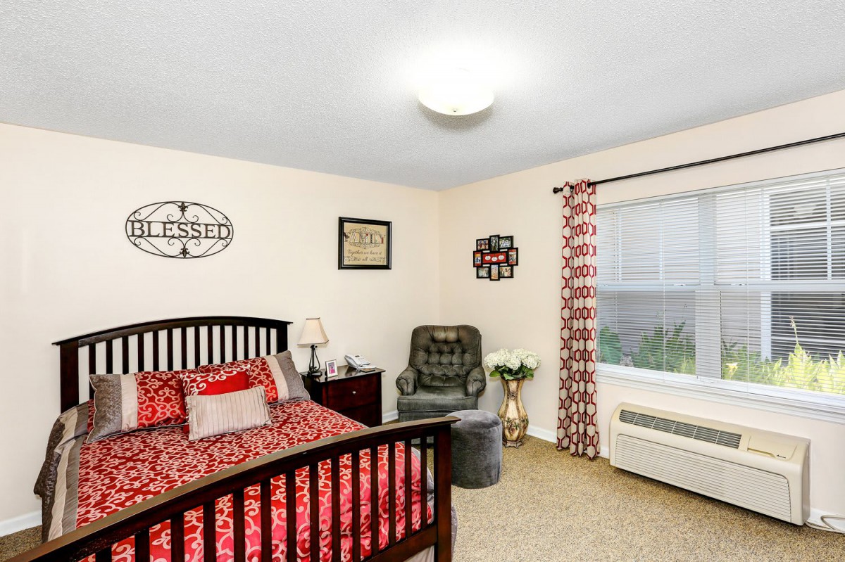A cozy bedroom with a red and black patterned bedspread, a comfortable armchair, and decorative accents.