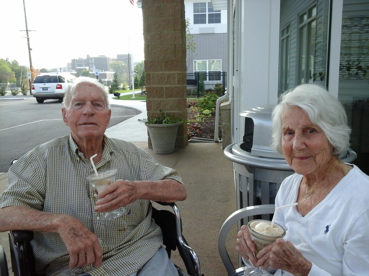 An elderly couple enjoying drinks while sitting outside.