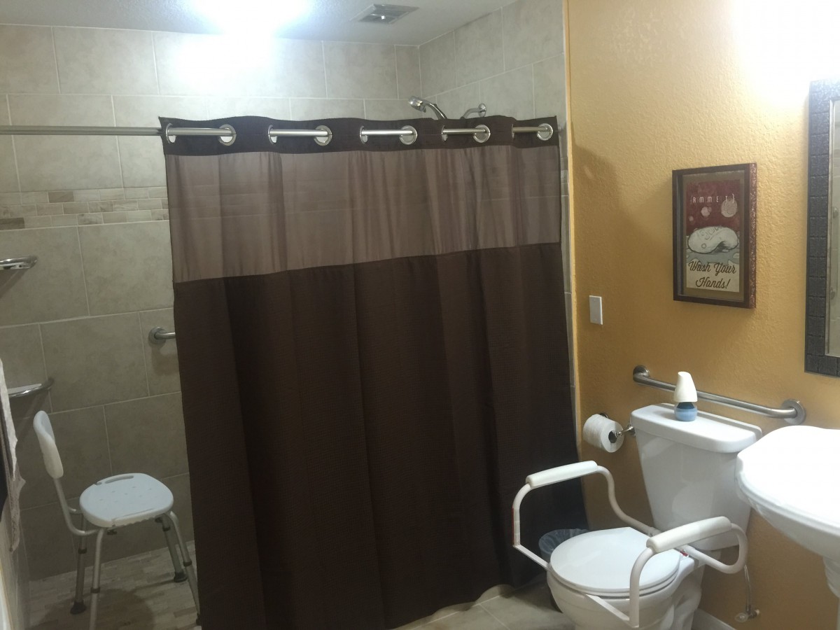 An accessible bathroom with a shower curtain, toilet, and supportive handrails.