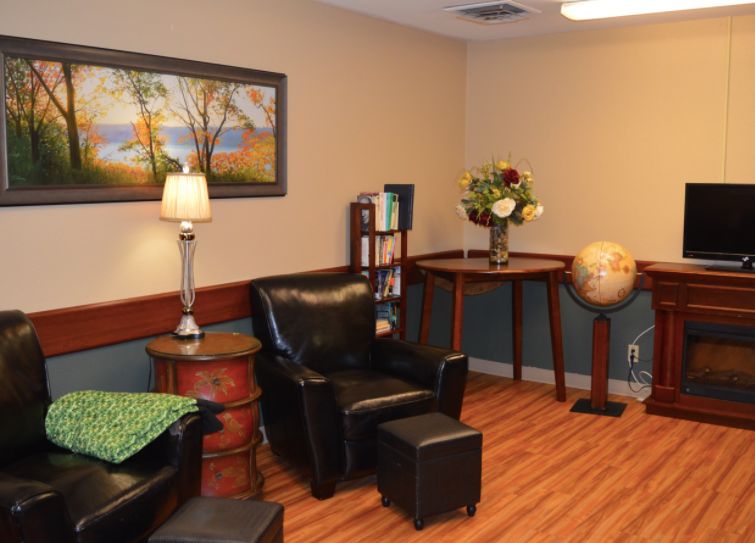 A cozy living room with an armchair, lamp, and decorative items such as a painting, bookshelf, and globe.