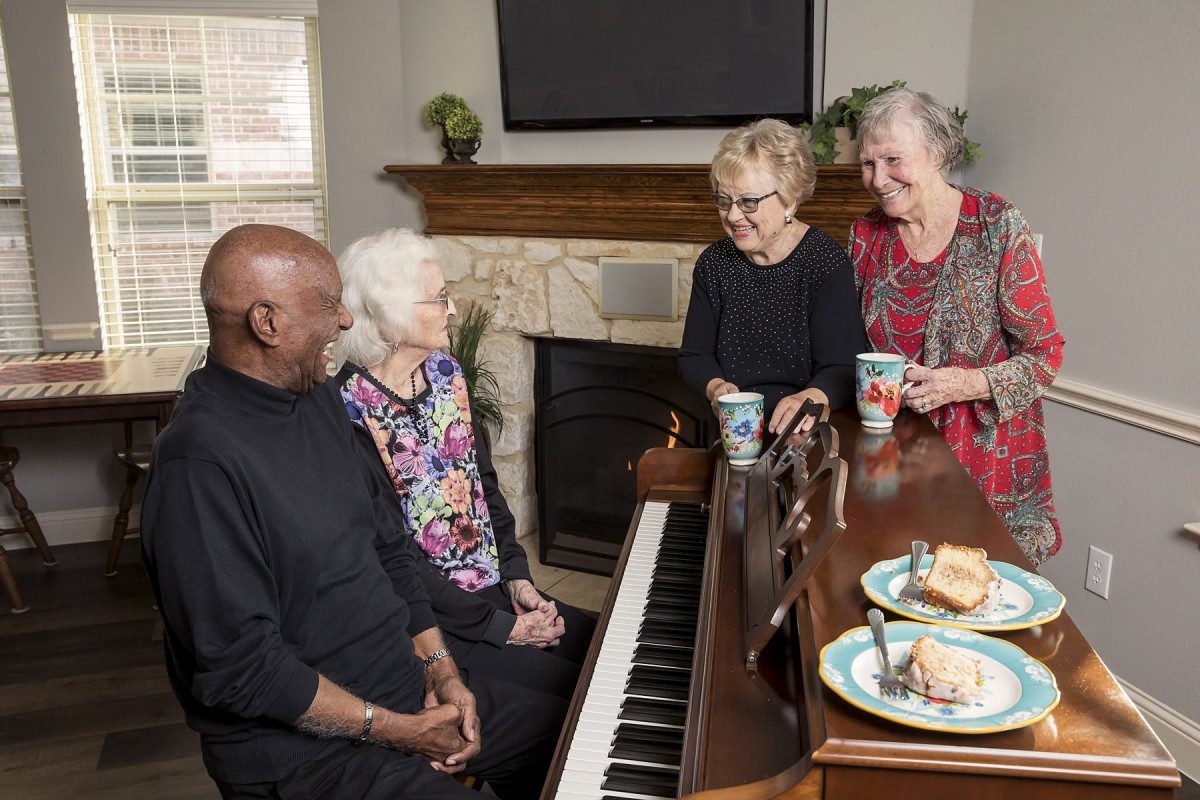A group of seniors enjoying coffee and conversation around a piano.