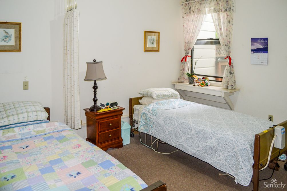 A cozy bedroom featuring two twin beds, a nightstand with a lamp, and a window with floral curtains.
