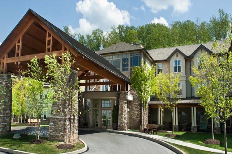 A modern residential building with a covered entrance surrounded by trees and greenery.