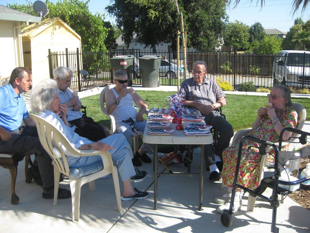 A group of seniors sitting outdoors, enjoying a sunny day together while socializing around a table.