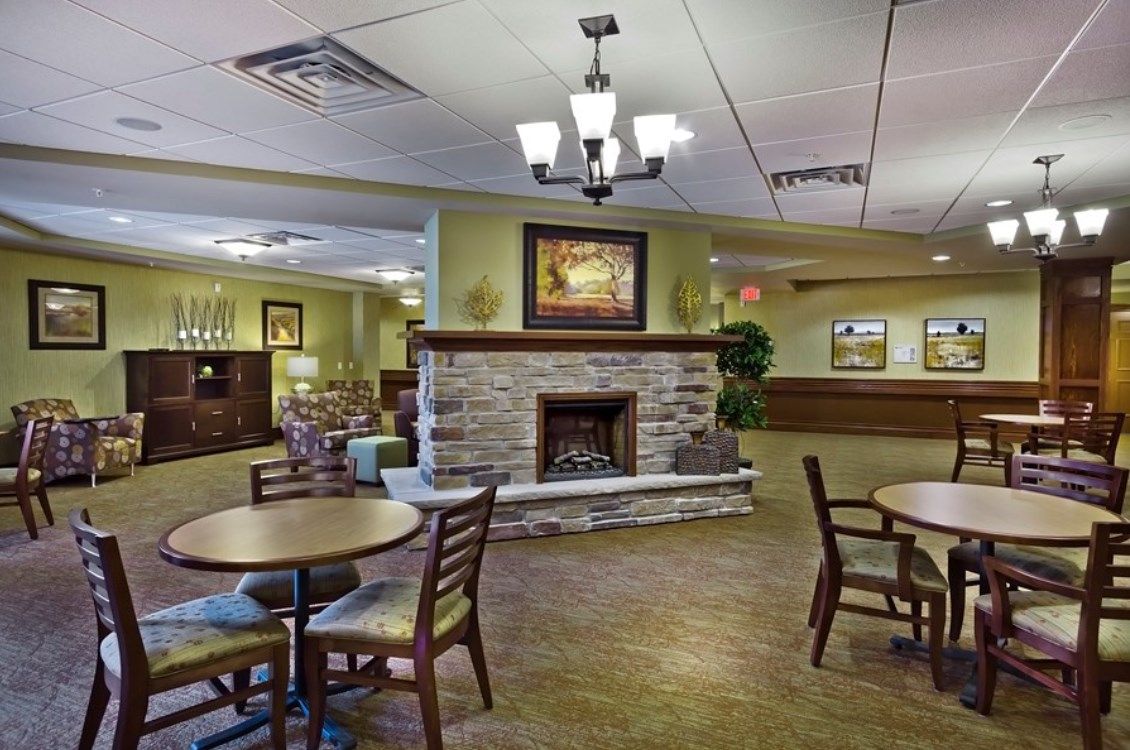 A cozy lobby with a stone fireplace, surrounded by tables and chairs, featuring decorative lighting.