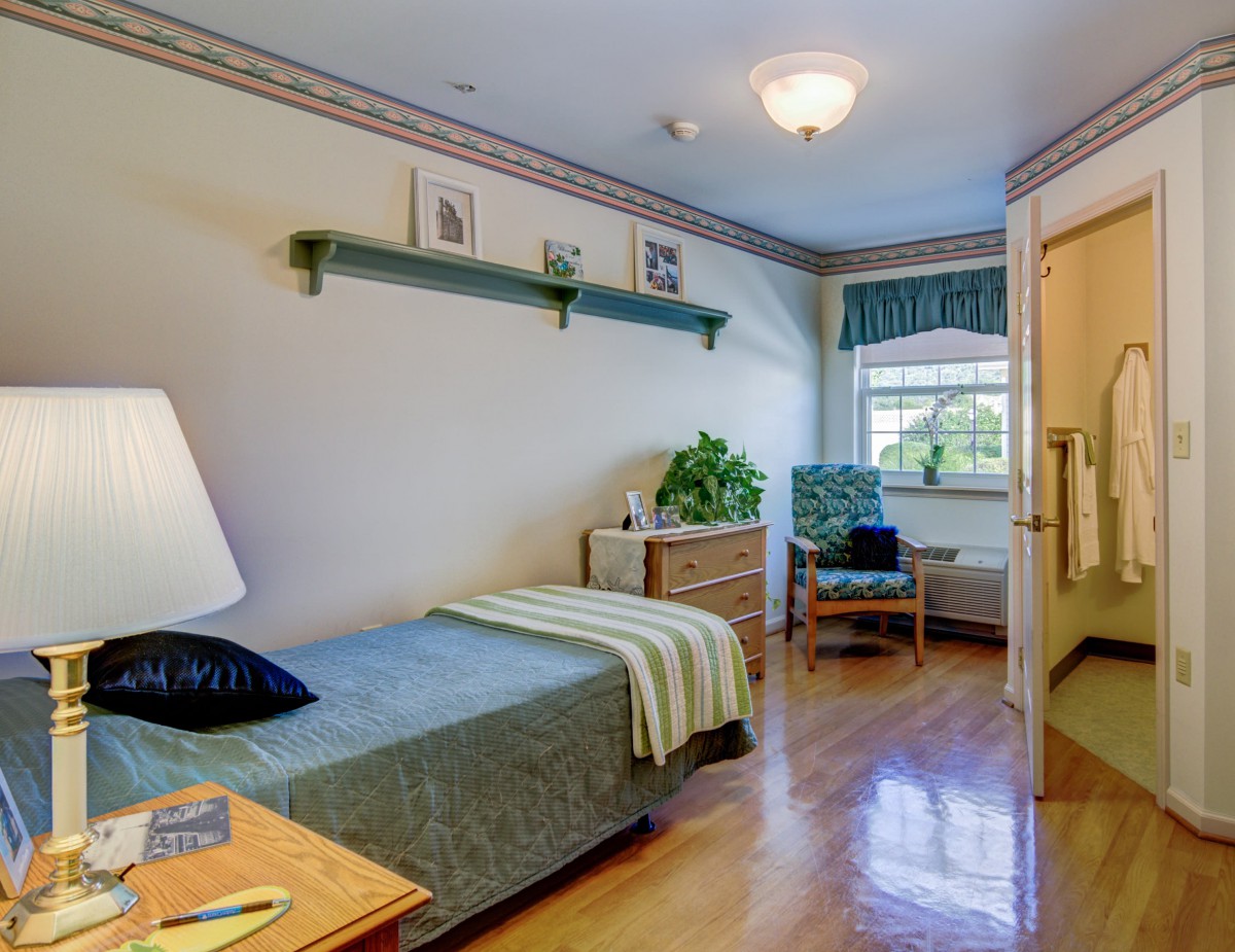 A cozy bedroom with a single bed, wooden flooring, and a window letting in natural light.