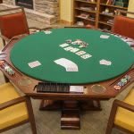 A round poker table with playing cards and chairs set up for a game.