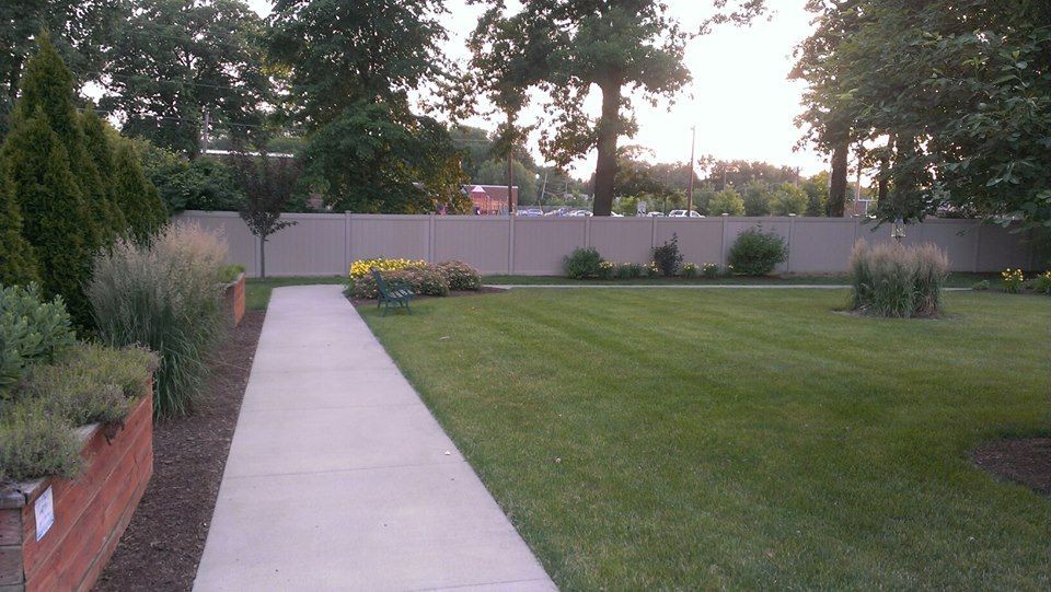 A well-maintained lawn with a concrete pathway and surrounding trees.
