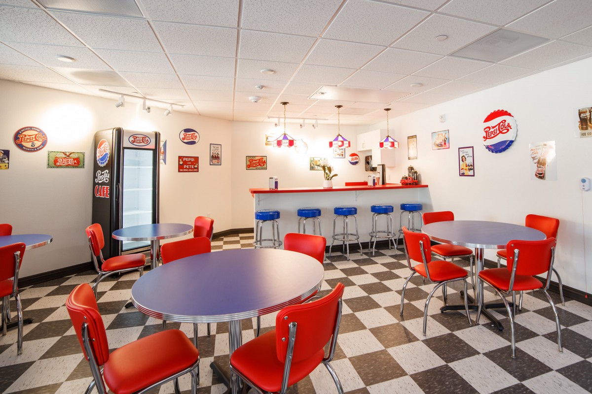 A retro-style diner interior with red chairs, checkered flooring, and a counter with bar stools.